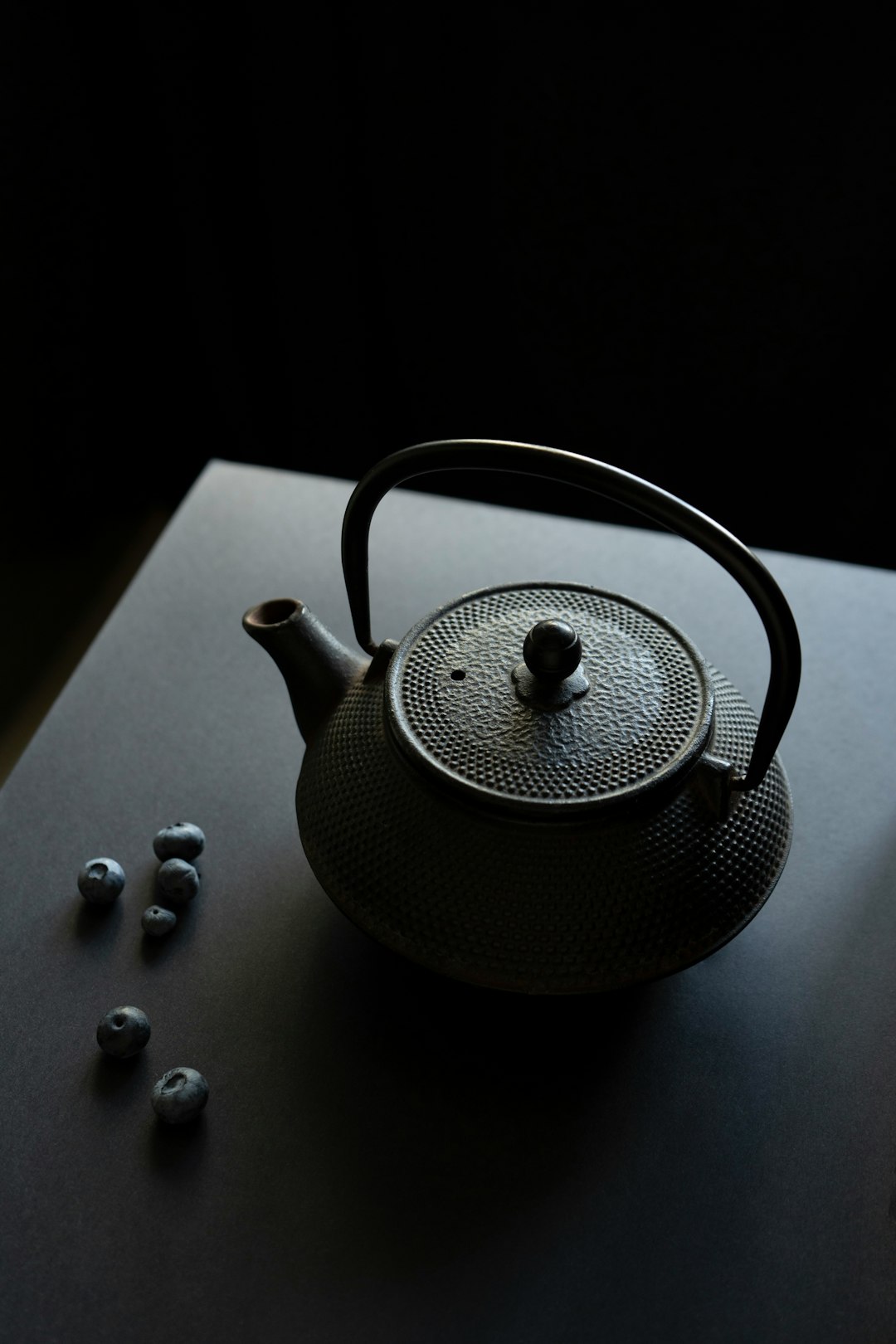 Black teapot on black background with blackberries.